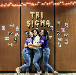 A photo of three Sigma Sigma Sigma sorority sisters hugging and posing for a picture together in the board rooms at Saint Leo’s University Campus